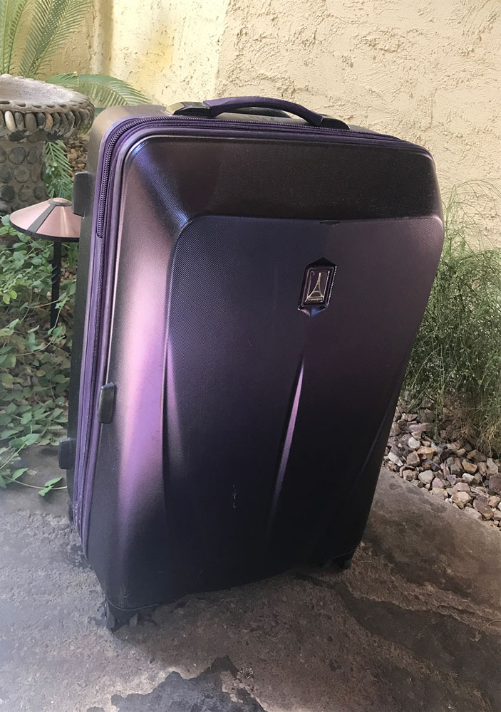 Purple hard case suitcase sitting on the ground demonstrated in a gift guide for international travelers. 