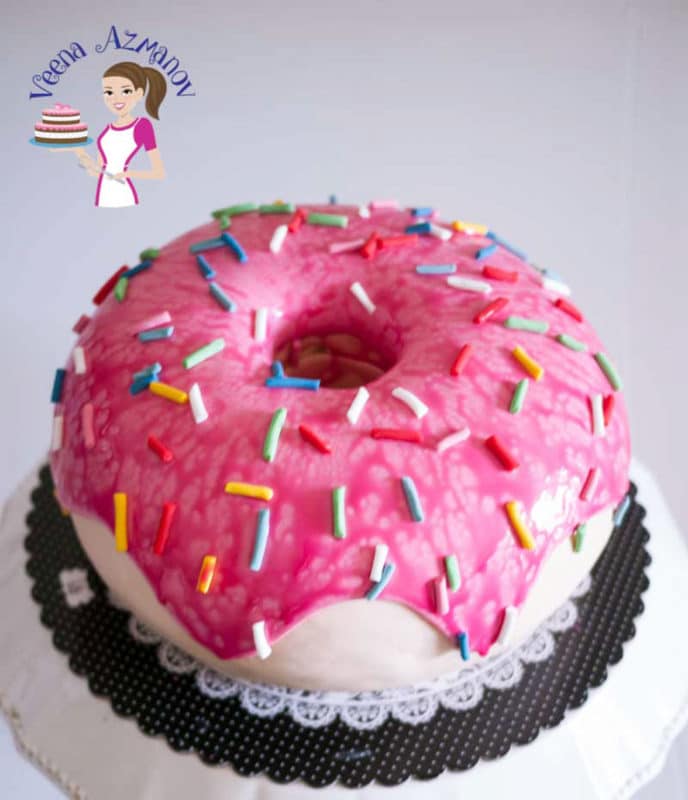 Pink donut cake topped with pink icing and colored sprinkles. 