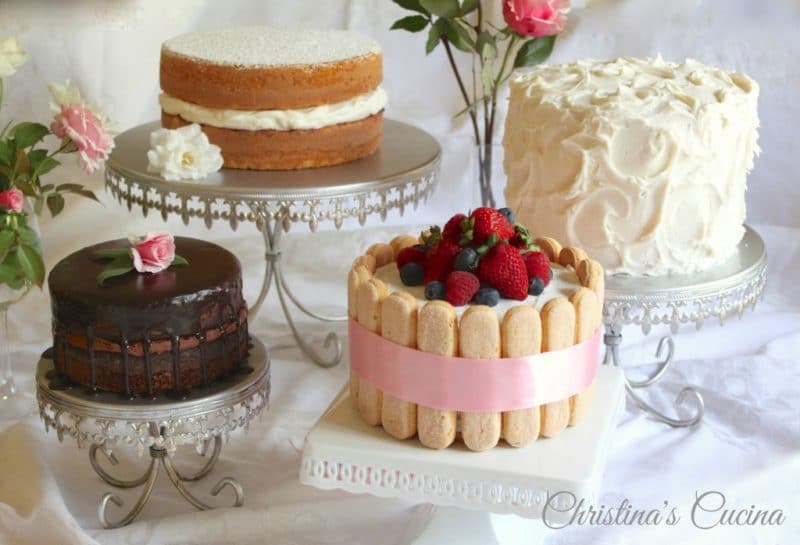 Display of 4 cakes: one chocolate, one white with berries and lady fingers, Once with white whipped frosting and a 2 tiered double cake.