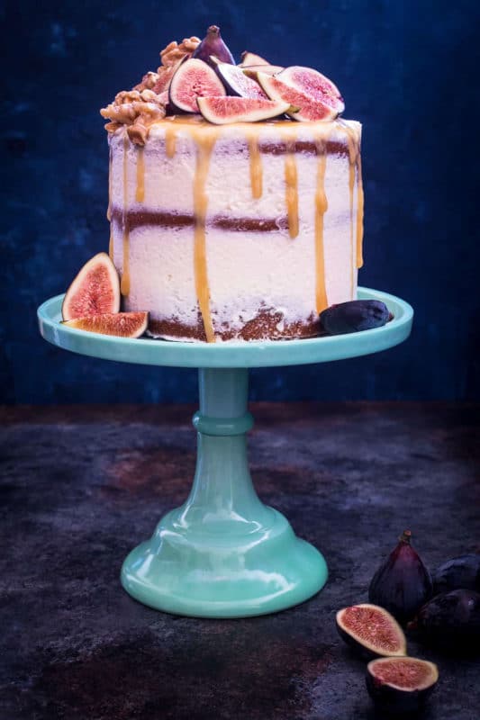 3 tiered Honey Walnut Fig Cake sitting on a blue cake display topped with figs, honey dripping down cake. 