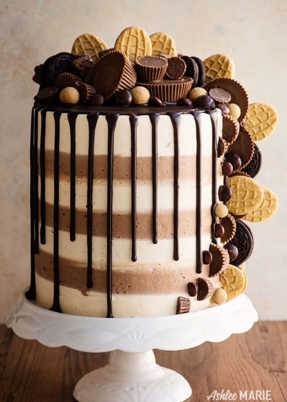 4 tiered peanut butter custom cake topped with nutter butters, chocolates and peanut butter candies, chocolate dripping down side of cake. 