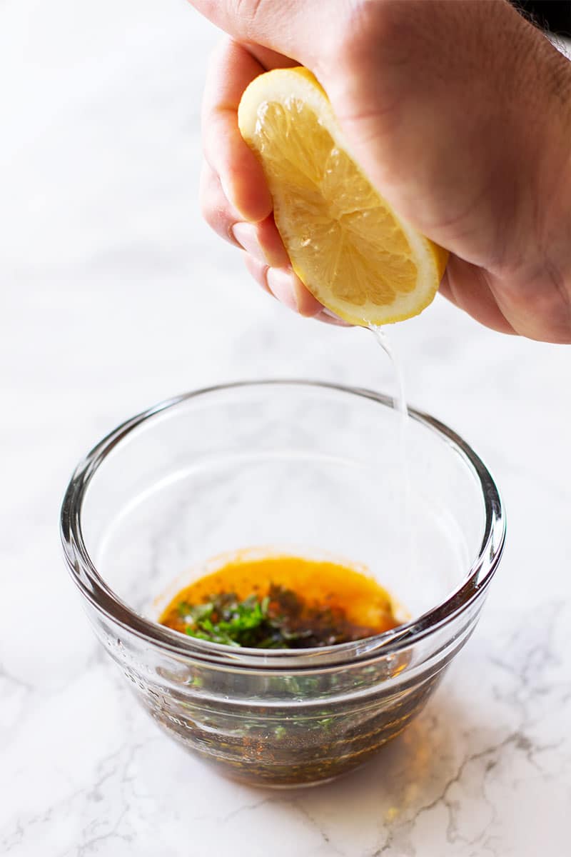 Hand squeezing a lemon into a glass bowl for a lemon herb marinade. 