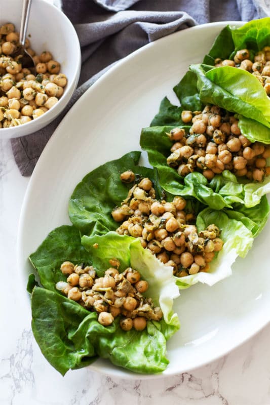 White dish containing 4 Pesto Chickpea Lettuce Wraps sitting on a white marble table. 