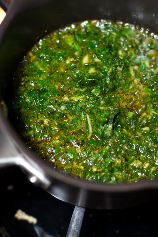 Homemade pesto sauce heating in a saucepan on a stove.