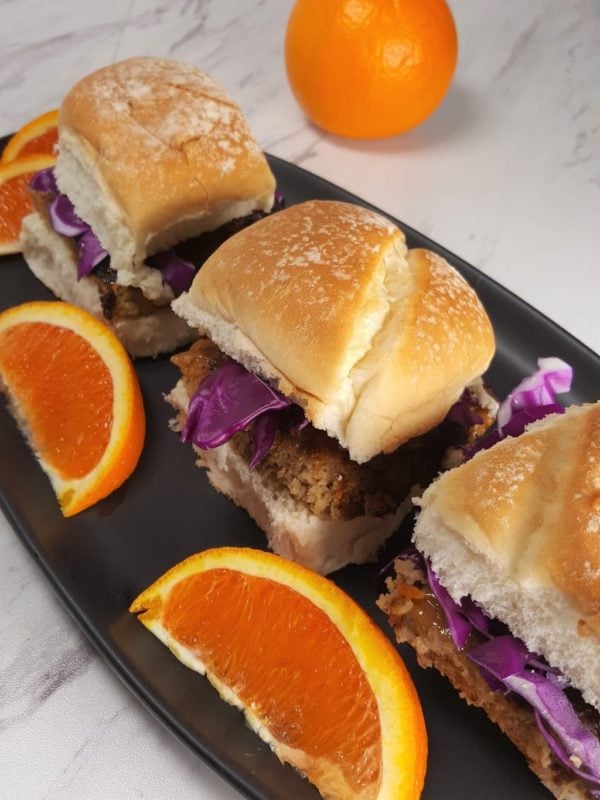 Black plate containing 3 Air Fryer Orange Turkey Burgers With Orange Aioli with purple cabbage and orange slices.