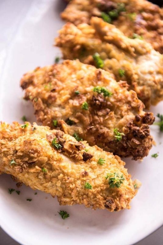 White plate containing 4 Air Fryer Potato Chip Chicken breasts topped with parsley.