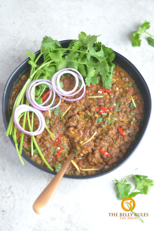 Instant Pot Dal Makhani black and kidney bean mix in a black bowl topped with onions and cilantro.