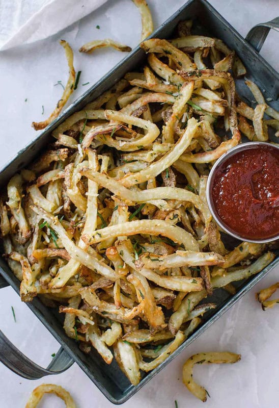 Metal pan containing air fried french fries topped with Parmesan cheese and parsley, ketchup on side.