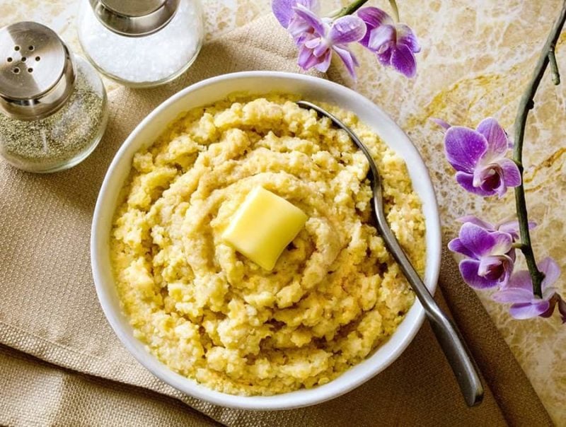 White bowl of polenta topped with butter, spoon in bowl.