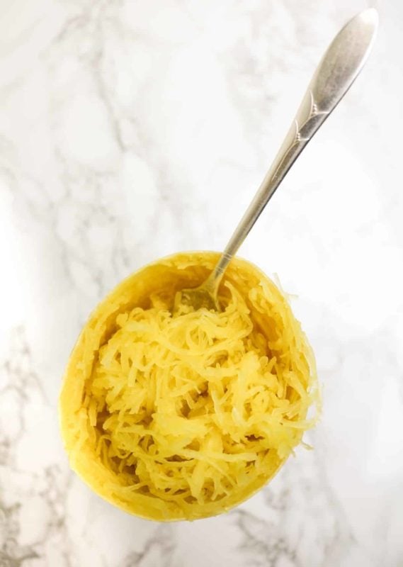 Spaghetti squash sitting on a marble table, fork in squash.