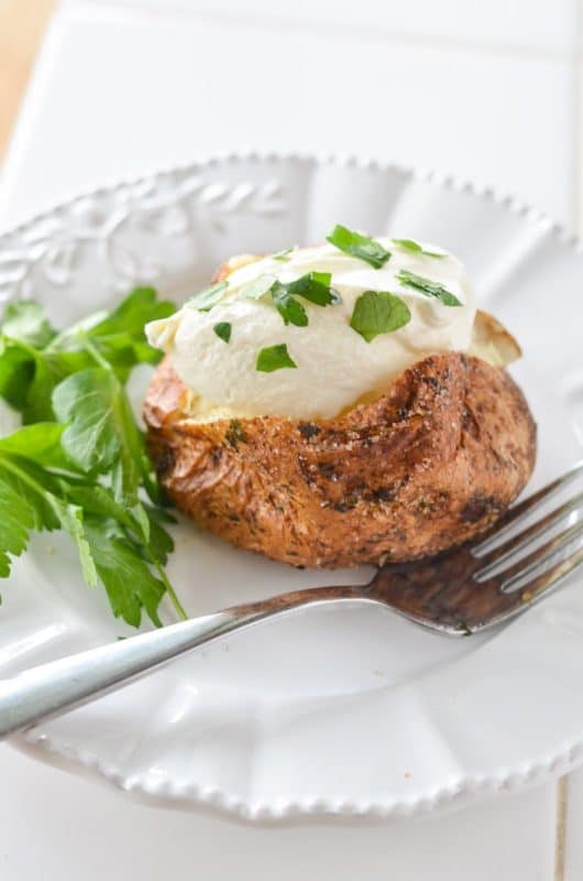 White plate containing an Air Fryer Baked Potato topped with sour cream and chives, fork on side.