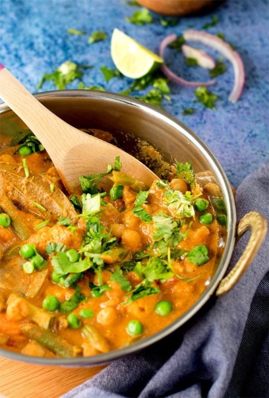 Silver bowl filled with Chickpeas and Vegetable Korma, topped with scallions and cilantro.