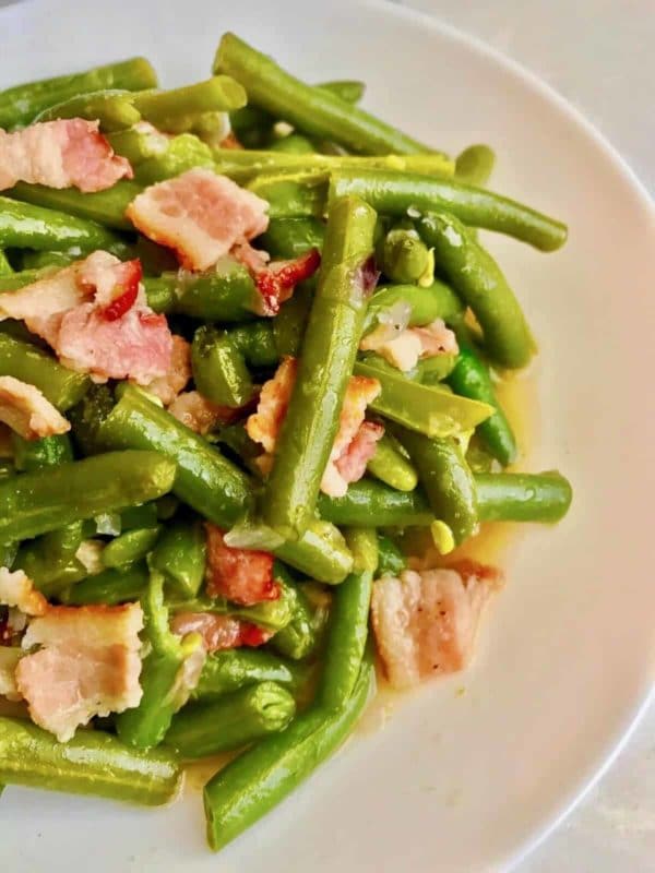 Cooked Green beans with bacon in a white plate cooked in an Instant Pot.