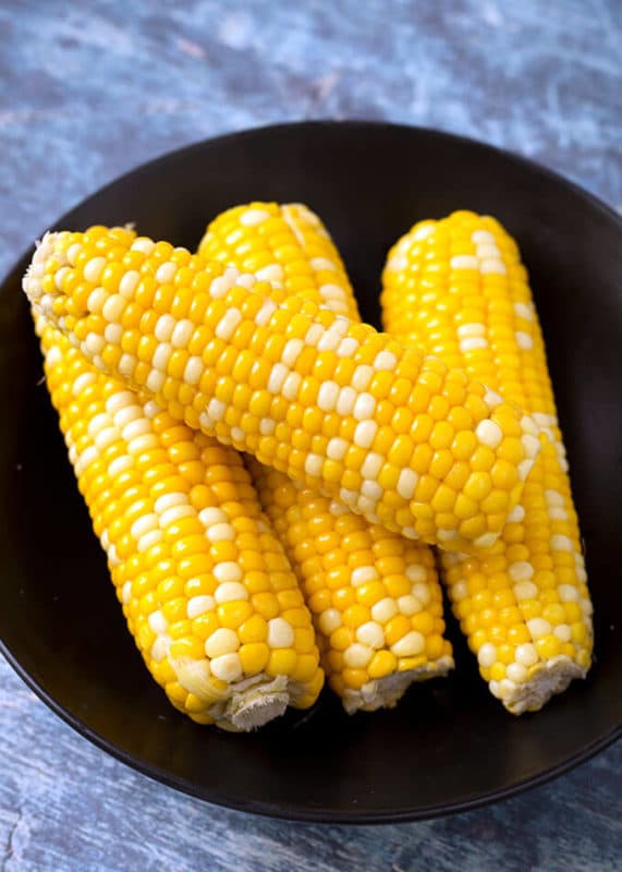 4 cobs of corn on a black plate sitting on a wooden table.