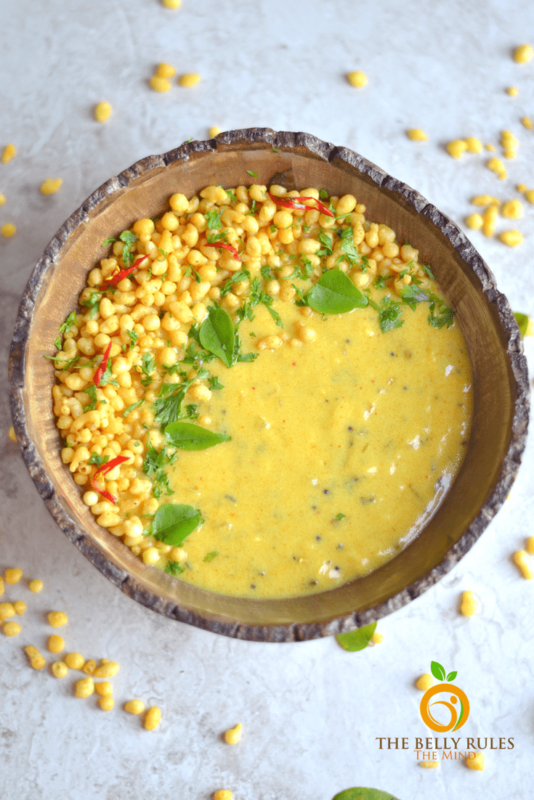Brown bowl containing Punjabi Kadhi Pakoda, kernels of corn on table.