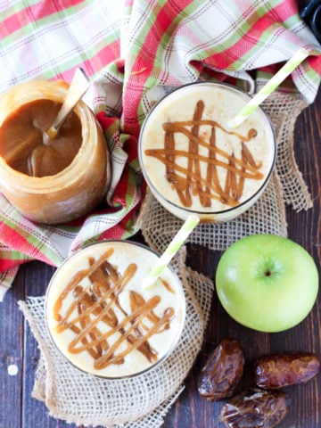 2 classes of Caramel Apple Protein Smoothie on a wooden table, caramel sauce, dates and green apples on table.