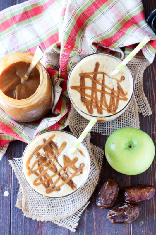 2 classes of Caramel Apple Protein Smoothie on a wooden table, caramel sauce, dates and green apples on table.