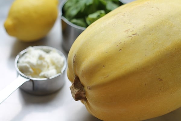 A whole spaghetti squash with a cup of goat cheese, fresh lemon and arugula in the background.