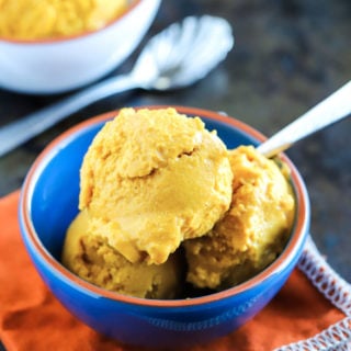 Blue bowl containing 3 scoops of pumpkin gelato, spoon in bowl.