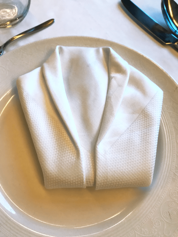 White napkin folded in the shape of a suit jacket on a dinner plate on The Disney Wonder Cruise.