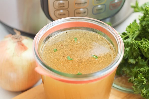 Cup of bone broth, onion, parsley and Instant Pot on table.