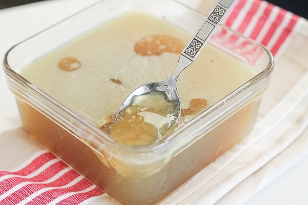 Chilled bone broth in a glass container with a gel consistency, spoon in broth.