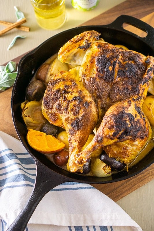 Cast iron skillet containing a roasted apple cider spatchcock chicken with orange and potatoes.