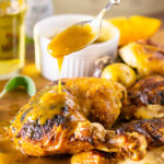 Roasted apple cider spatchcock chicken on a brown table, spoonful of savory sauce dripping onto chicken.