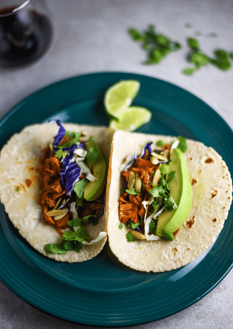 Teal plate on a table containing 2 jackfruit tacos topped with purple cabbage and avocado. 