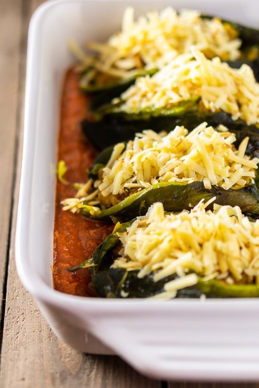 Pasilla peppers stuffed with chorizo and butternut squash and topped with cheese in a pan with ranchero sauce. 