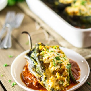 A single chorizo-butternut squash chile relleno on a plate with ranchero sauce. In the background is the pan, plate, forks and cilantro.