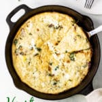 a slice of Hearty Spinach Frittata on a white plate with a fork slicing into it. A serving utensil and cast iron skillet are in the background.