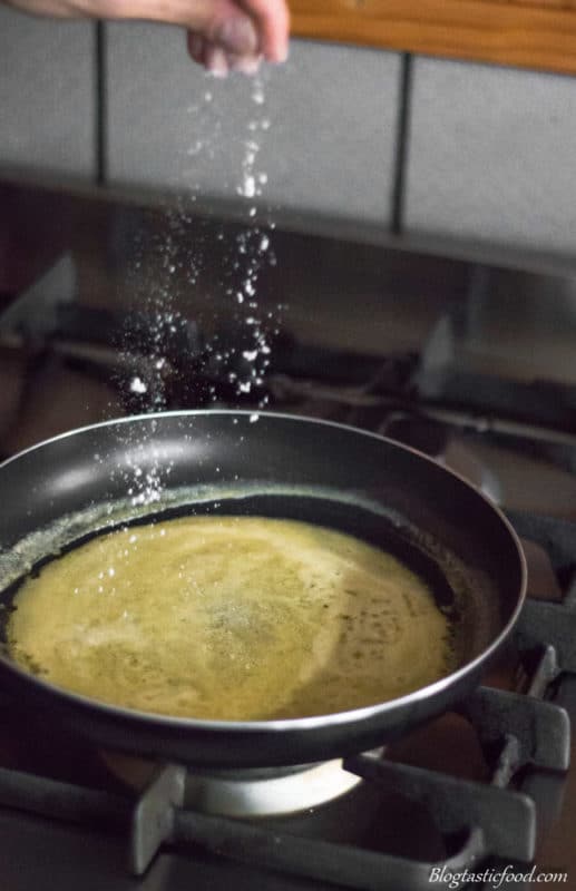 Someone seasoning an emulsifying butter sauce with salt.