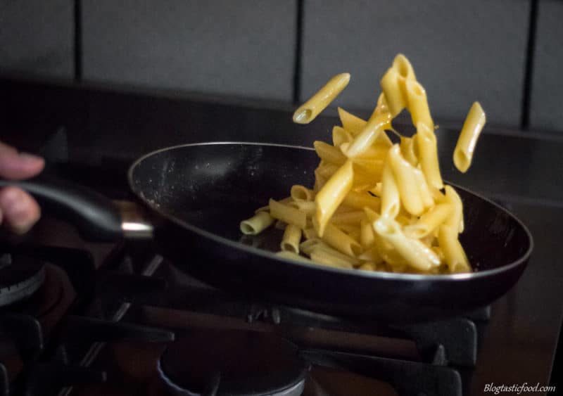 Someone tossing gluten free pasta in butter sauce.