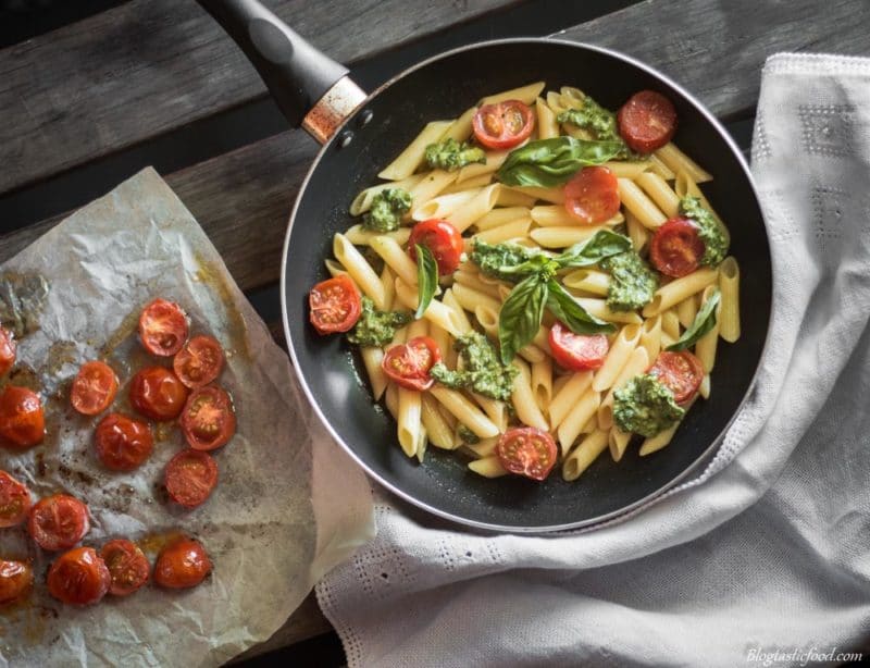 An overhead photo of gluten free pasta served with pesto and roasted cherry tomatoes.