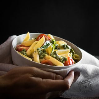 A white bowl filled with guten free pasta, pesto and cherry tomatoes.