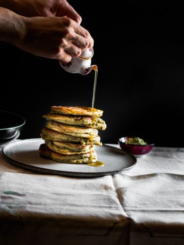A photo of stacked matcha gluten free pancakes with lemon and maple sauce being poured over the top.