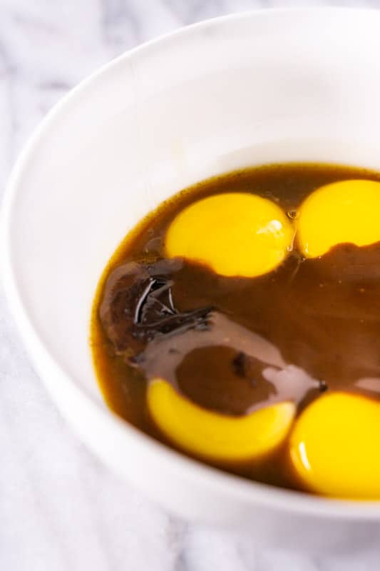 A white bowl with egg yolks and the cream mixture to temper the eggs.