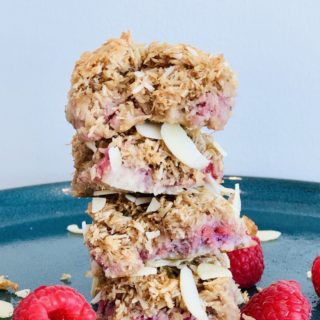 coconut raspberry bars and raspberries stacked on a green plate
