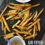 Air Fryer French Fries topped with Parmesan cheese and fresh parsley on a black cutting board.