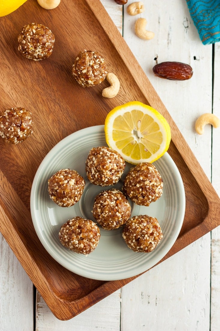 A plate of lemon bliss balls on a wooden board with lemon slices and dates.