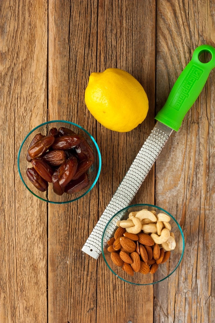 A bowl of dates, nuts, a lemon and a zester on a wooden board.