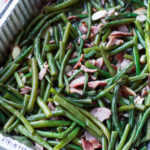 Aluminum pan containing green beans topped with bacon.