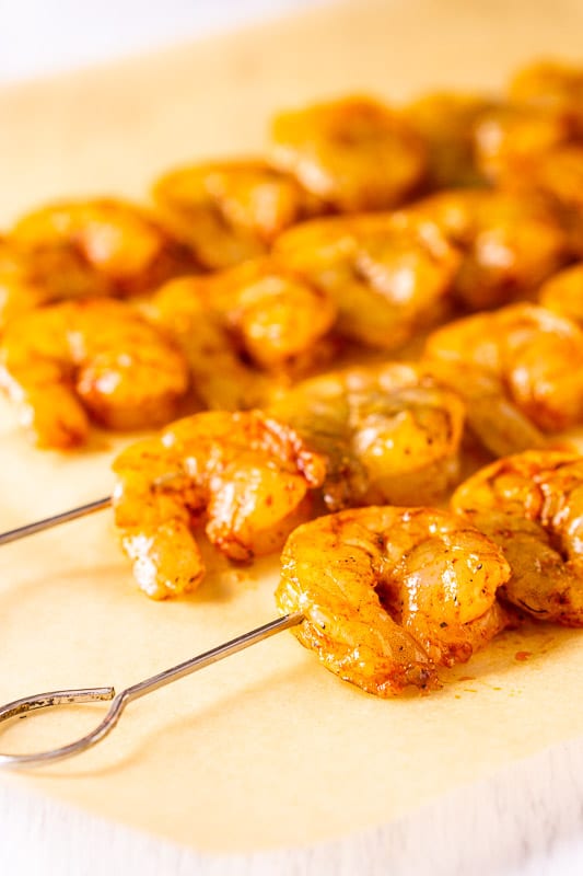 Shrimp threaded onto skewers and set on top of parchment paper before grilling.