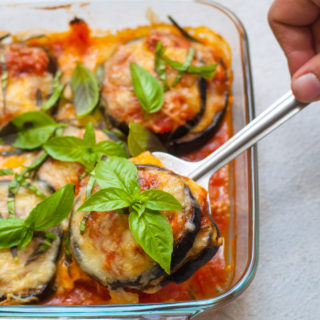 Glass baking dish containing a spoonful of eggplant parmesan topped with cheese and fresh basil.