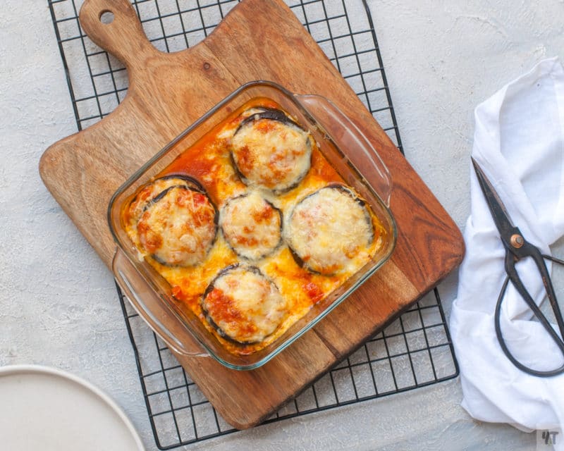 Baked eggplant topped with mozzarella and Parmesan cheese in a glass baking dish.