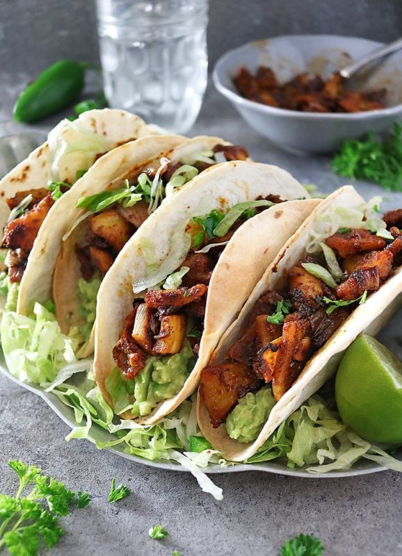Spicy jackfruit tacos topped with lettuces and lime.