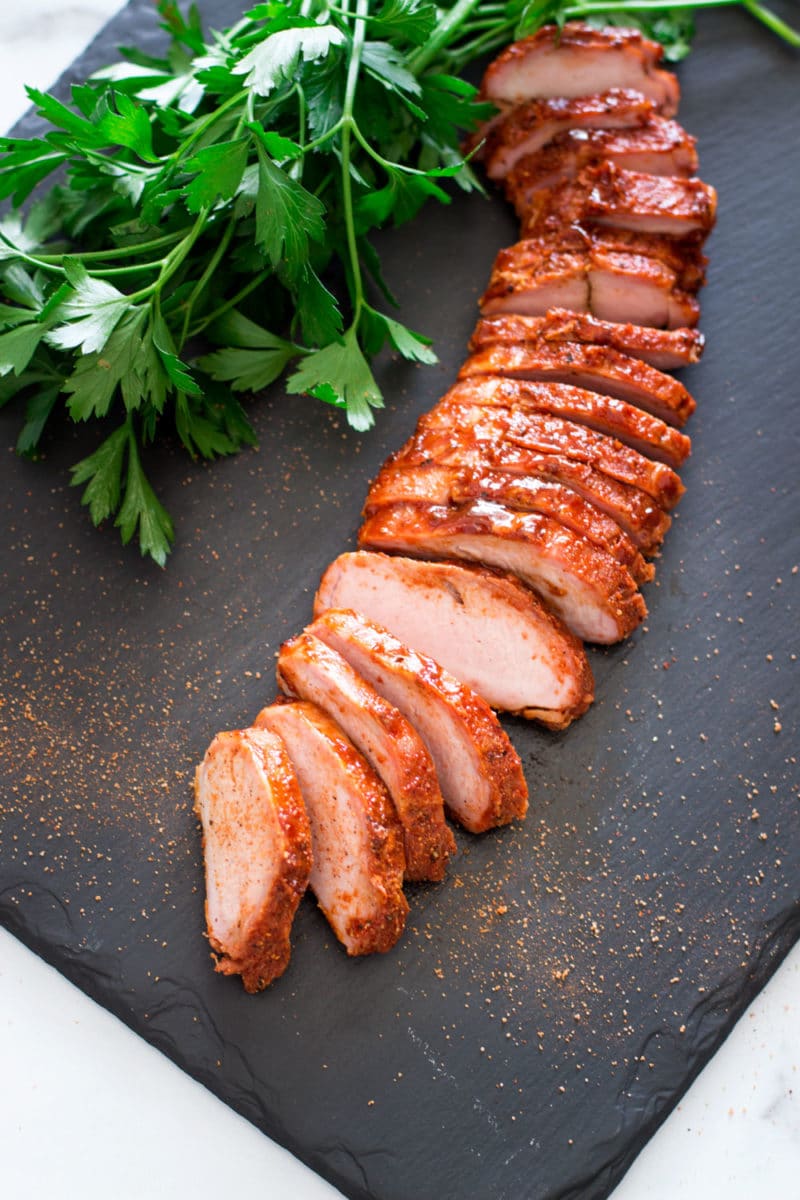 Sliced pork on a black slate tray, topped with spiced rub.