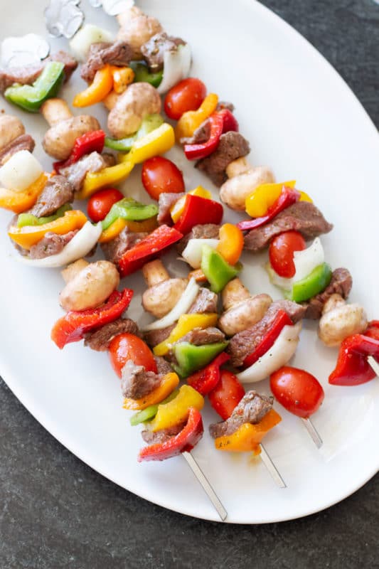 White platter containing four steak and vegetable skewers.