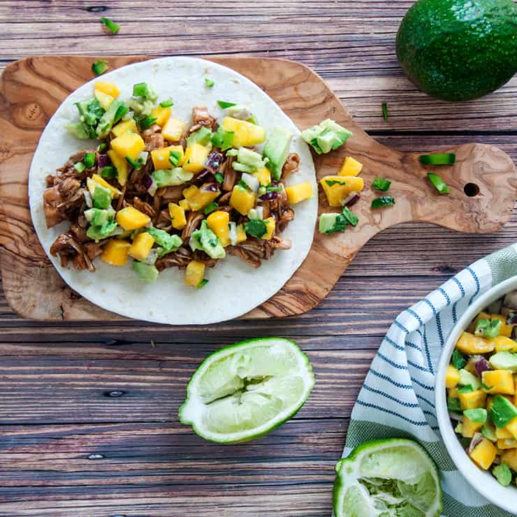 Vegan tacos topped with a mango salsa, limes on table.